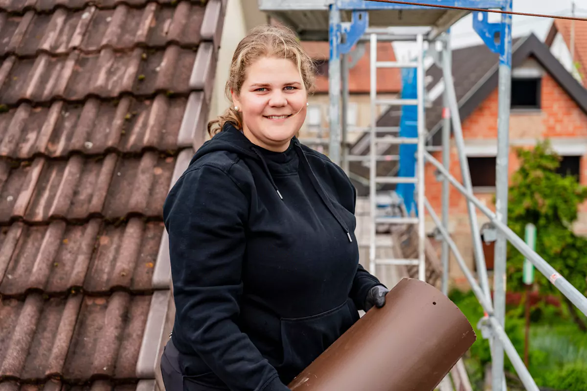 junge Frau mit Dachziegel in der Hand steht auf einer Baustelle und lächelt