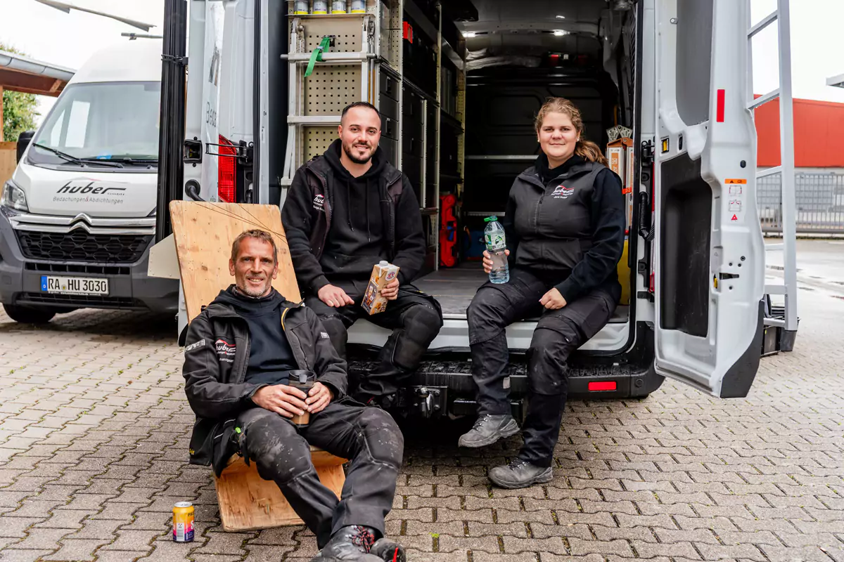 3 Handwerker:innen machen eine Pause und sitzen im Heck eines Sprinters
