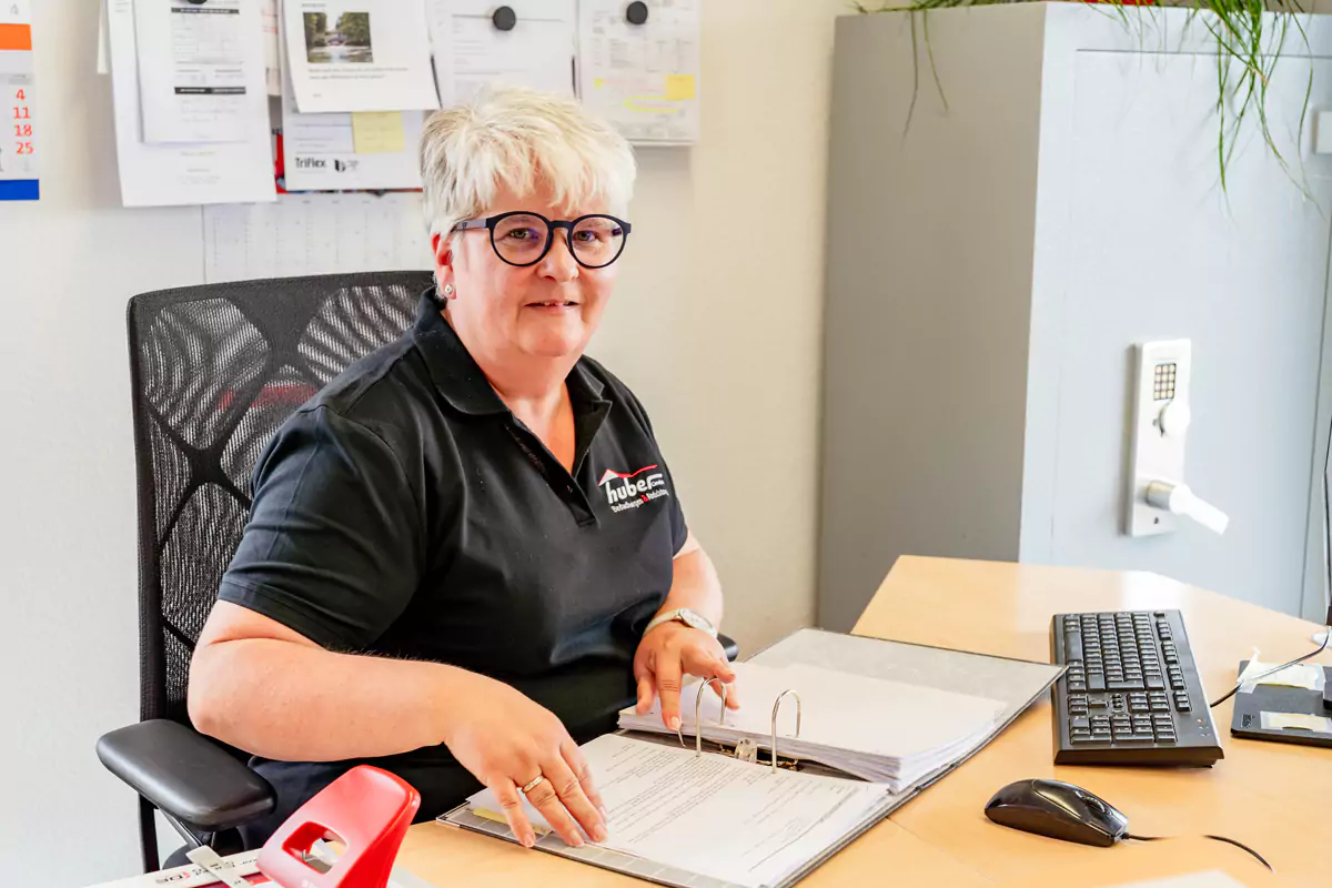 Frau mit kurzen blonden Haaren und Brille prüft Daten in einem Aktenordner