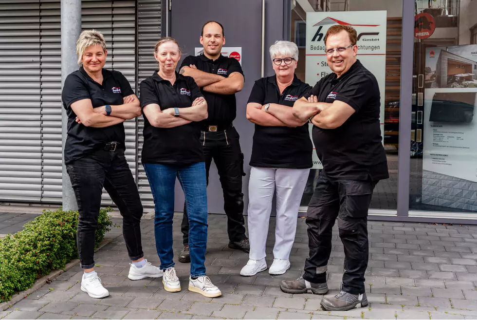 Teamfoto 5 Mitarbeiter:innen stehen mit verschränkten Armen vor dem Eingang des Firmengebäudes