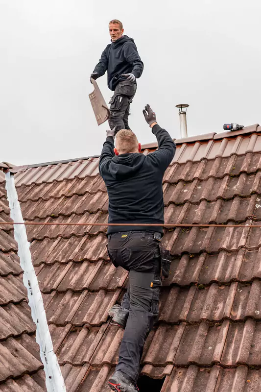 2 Dachdecker auf einem Dach werfen sich einen Dachziegel zu