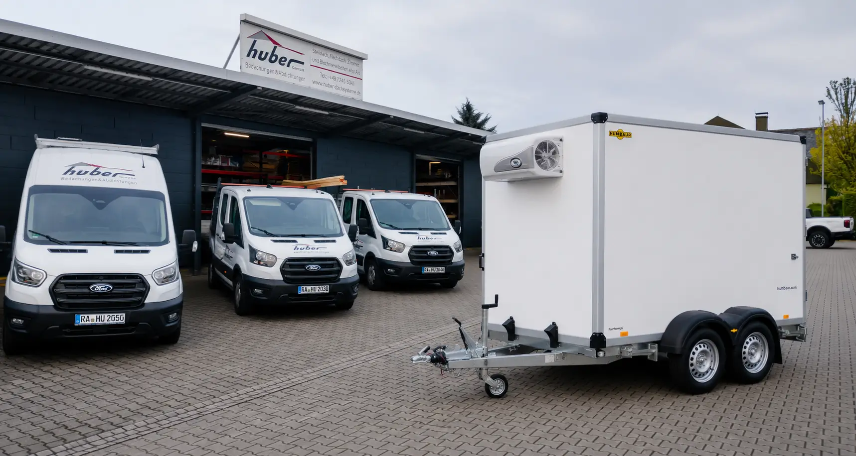 Kühlanhänger auf gepflastertem Firmengelände vor mehreren geparkten Fahrzeugen